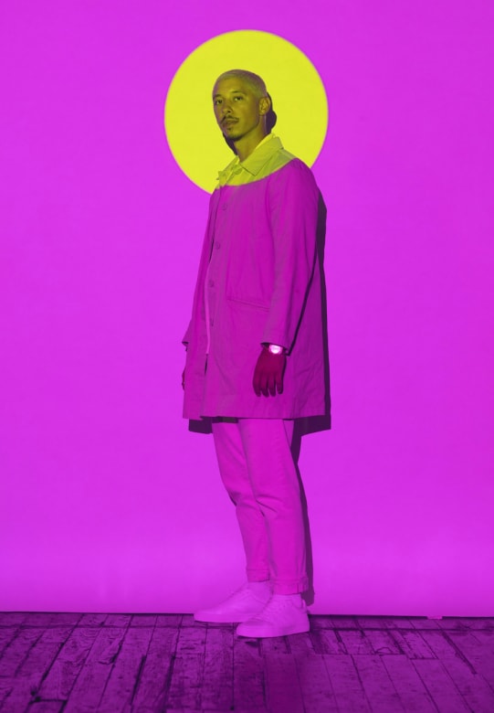 man standing against wall lit in pink with yellow spotlight around his head